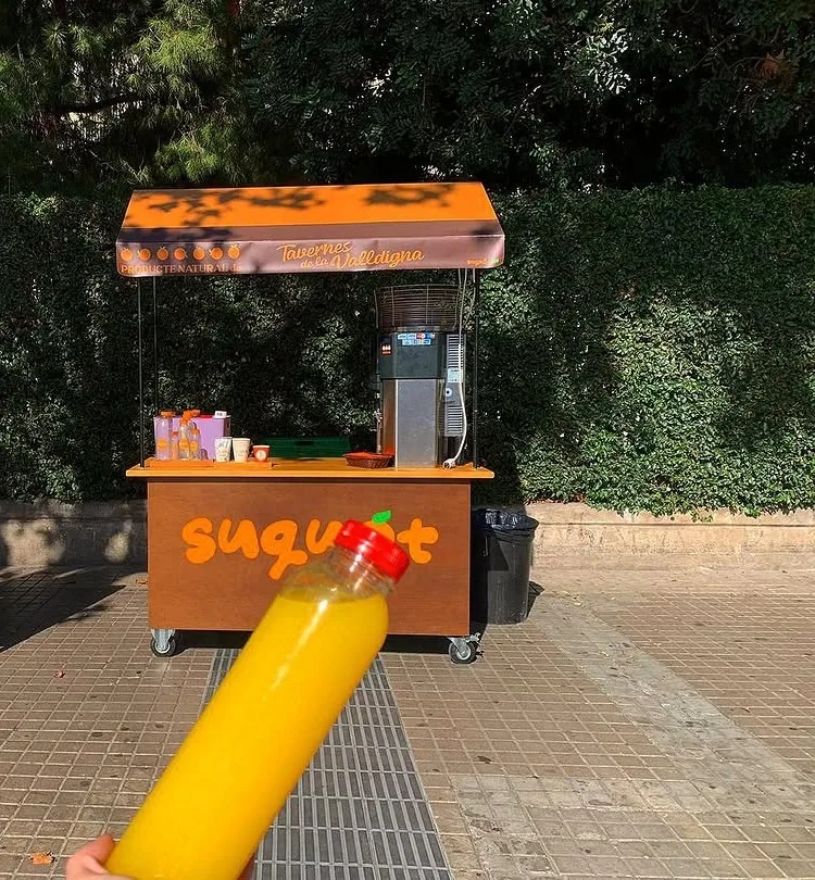 Botella de zumo de naranja recién exprimido delante de nuestro carrito, con el toldo de Tavernes de la Valldigna