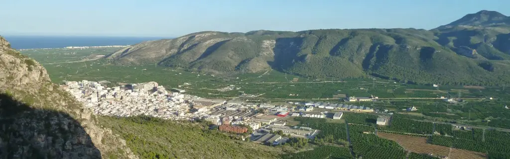 Vista panorámica de La Valldigna: campos de naranjos entre montañas, con el mar al fondo